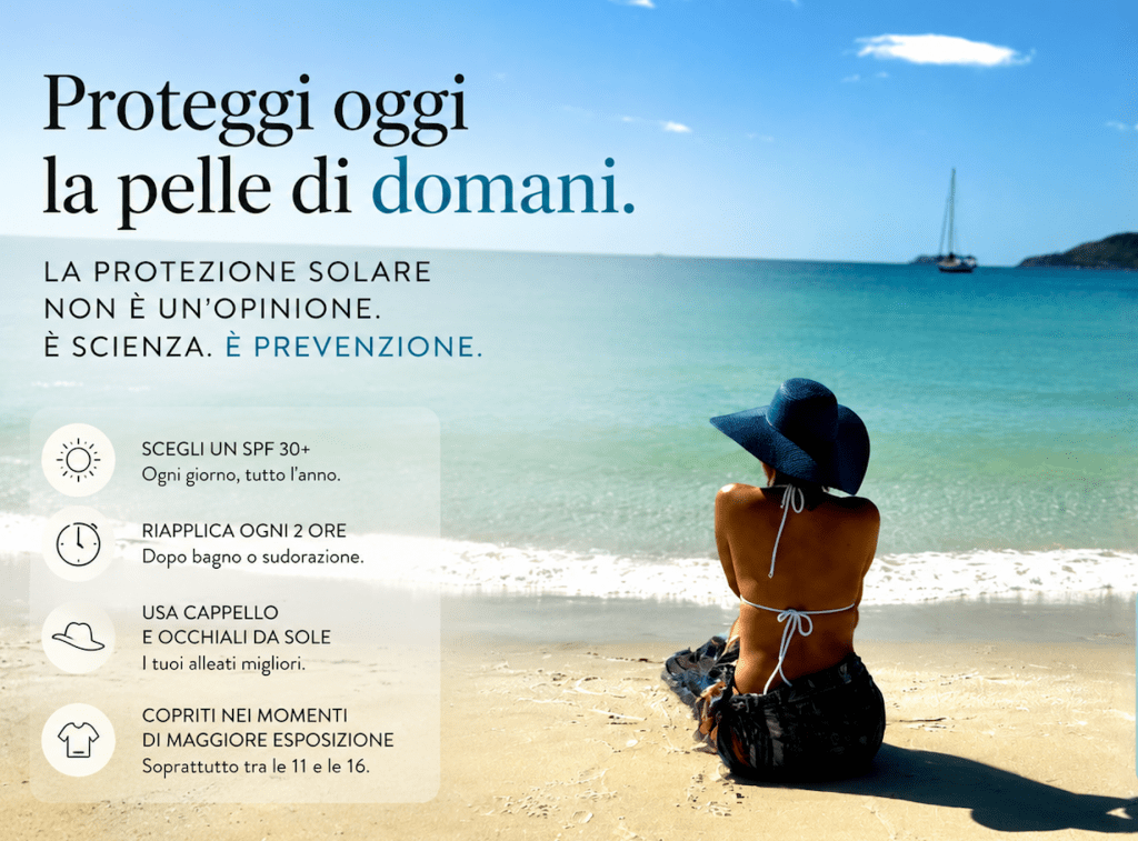 Scena estiva sulla spiaggia con donna di spalle e cappello a tesa larga davanti al mare turchese. L'immagine richiama l'importanza della protezione solare quotidiana attraverso l'uso di barriere fisiche come cappelli, ombra e abbigliamento adeguato.